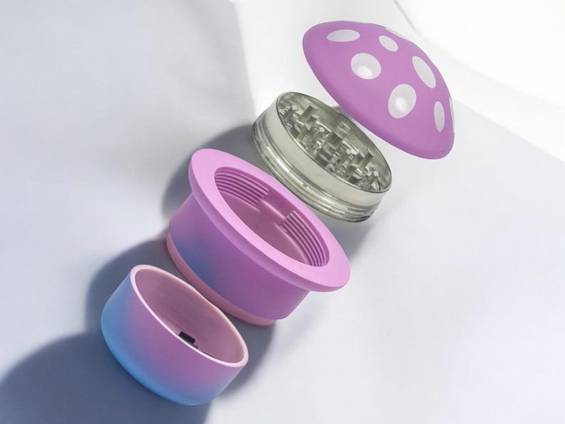 Exploded view of a pink and blue mushroom grinder with four separate parts, including a polka-dot cap, metal teeth chamber, filter, and storage – a cute and funny spice grinder perfect for herbs or seasoning.