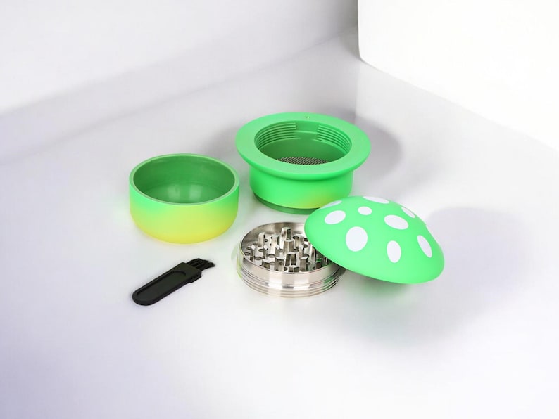 Cute green mushroom-shaped herb and spice grinder with four parts, including a metal grinding chamber, mesh screen, and cleaning brush – a funny and colorful grinder perfect as a unique kitchen or smoking accessory.