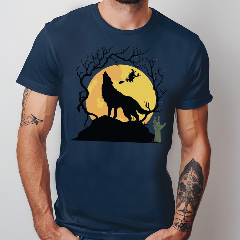May include: Navy blue t-shirt featuring a Halloween design. A black silhouette of a howling wolf is centered on a large yellow moon, with a witch flying on a broomstick. Bare tree branches and a green zombie hand complete the spooky scene.