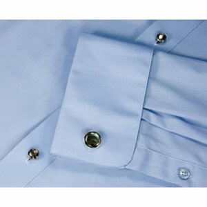 May include: A light blue dress shirt with a pair of cufflinks. The cufflinks are round and have a dark green and black iridescent finish.