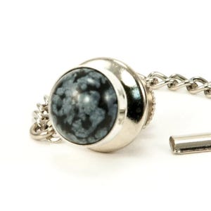 May include: A silver tie tack with a round, black and gray snowflake obsidian stone.