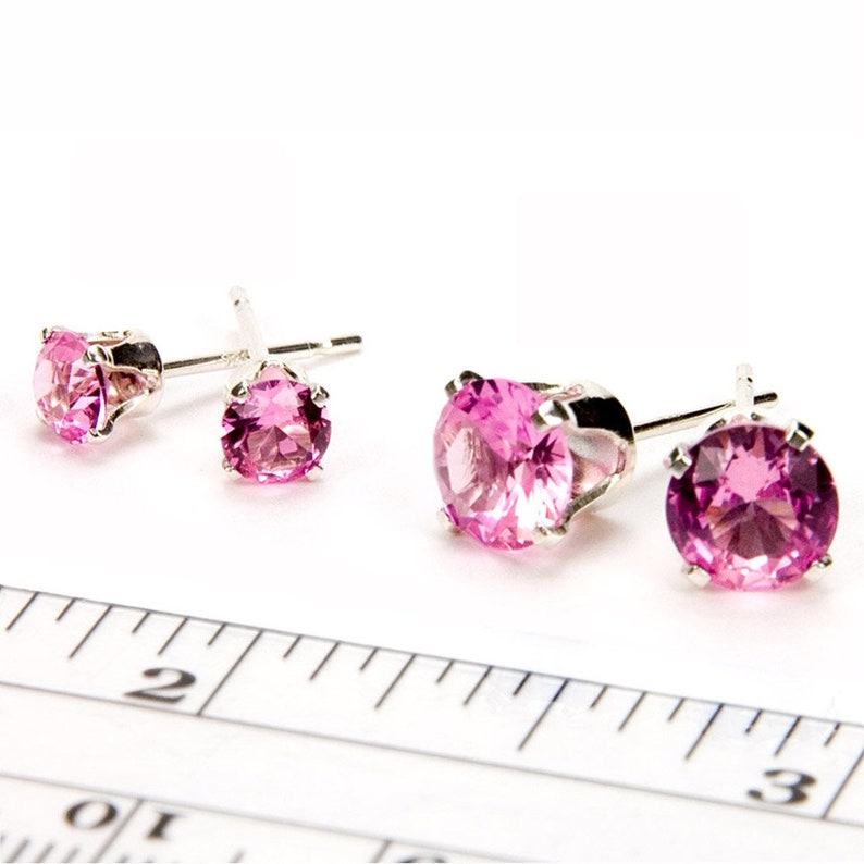 May include: A set of three pink gemstone earrings with silver settings. The earrings are shown on a white surface with a ruler for size reference.