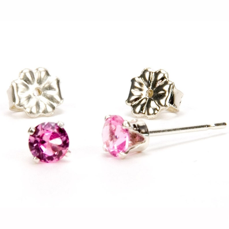 May include: A pair of silver stud earrings with pink gemstones. The earrings have a flower-shaped backing.