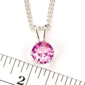 May include: A silver chain necklace with a pink gemstone pendant. The pendant is about 1/2 inch in diameter.