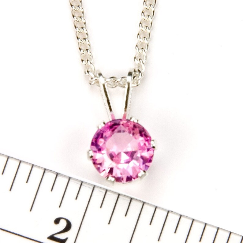 May include: A silver chain necklace with a pink gemstone pendant. The pendant is about 1/2 inch in diameter.