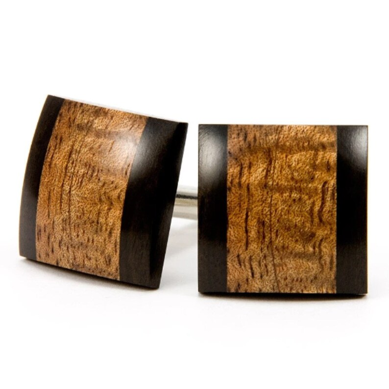 May include: A pair of square wooden cufflinks with a black inlay. The cufflinks have a wood grain pattern and a dark brown color.