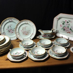 May include: A set of white porcelain dinnerware featuring a floral design in shades of pink and green. The set includes plates, bowls, a serving dish, and a gravy boat.