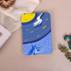 May include: A rectangular tablet case featuring a graphic illustration of a swimming pool at night. The design includes a yellow moon, a diving board, and swimmers in blue water. Text on the case reads Midnight Tonight, WPLM 97.7FM, WPLM.ORG, and midnight swim is back.
