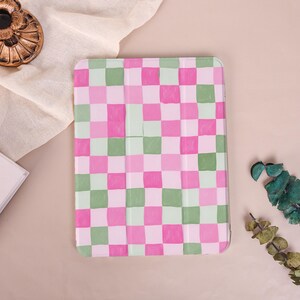 May include: A tablet case with a pink, green, and white checkered pattern. The case is rectangular and has a folding cover. The design is a grid of squares in varying shades of pink, green, and white.