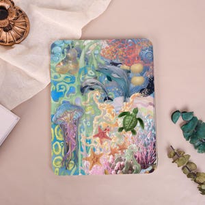 May include: A rectangular tablet case featuring a vibrant underwater scene with two dolphins, a purple jellyfish, a green sea turtle, and various starfish. The design includes colourful coral reefs, aquatic plants, and bubbles set against a blue background.