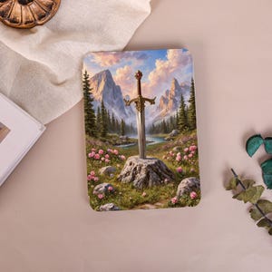 May include: A rectangular tablet case featuring a fantasy illustration of a metallic sword embedded in a stone stump. The scene includes a flowing river, green pine trees, jagged mountains, a cloudy sky, and pink flowers in the foreground.