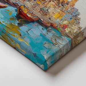 May include: A close-up of the edge of a canvas painting. The painting depicts a colorful cityscape with a blue body of water in the foreground. The paint is applied in thick, textured strokes, giving the painting a three-dimensional effect.