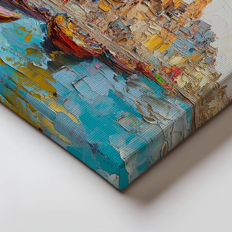 May include: A close-up of the edge of a canvas painting. The painting depicts a colorful cityscape with a blue body of water in the foreground. The paint is applied in thick, textured strokes, giving the painting a three-dimensional effect.
