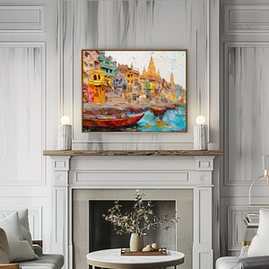 May include: A colorful painting of a cityscape with buildings and boats on a river. The painting is framed in gold and hangs above a fireplace.