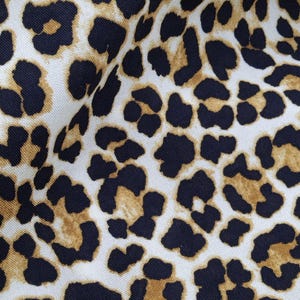 Puede incluir: Primer plano de una tela con estampado de leopardo. El diseño presenta manchas negras y manchas de color marrón claro sobre un fondo blanco. La tela está doblada, creando sombras y textura.