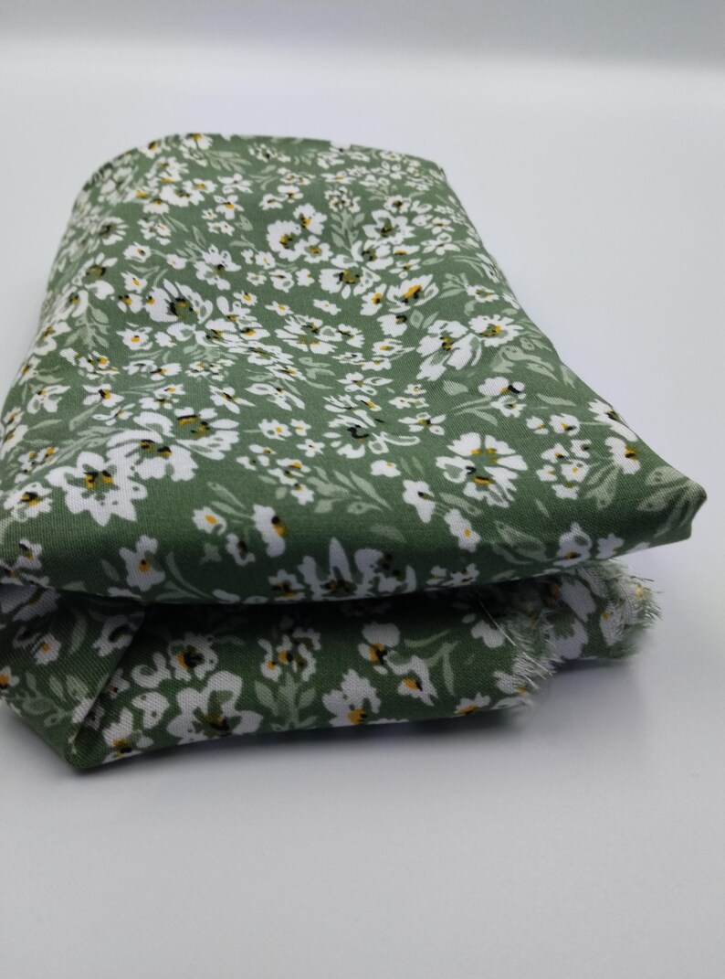 May include: Folded fabric with a green background and a white floral pattern. The fabric is a light green color with small white flowers and yellow centers. The fabric is folded over on itself.