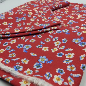 K&ouml;nnte beinhalten: Roter Stoff mit floralem Muster. Der Stoff ist mit kleinen blauen, wei&szlig;en und gelben Blumen bedeckt. Die Kanten des Stoffes sind ausgefranst und zeigen die rohe Kante des Materials. Der Stoff ist gefaltet.