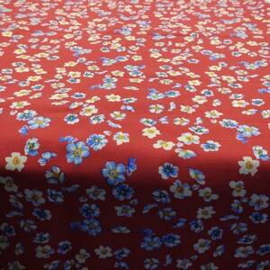 K&ouml;nnte beinhalten: Roter Stoff mit einem Muster aus kleinen blauen, wei&szlig;en und gelben Blumen. Das florale Design ist gleichm&auml;&szlig;ig &uuml;ber die Stoffoberfl&auml;che verteilt und erzeugt ein dichtes und farbenfrohes Muster.