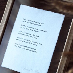 Könnte beinhalten: Gerahmter Druck mit einem Gedicht in schwarzer Schrift auf strukturiertem, cremefarbenem Papier. Das Gedicht ist signiert. Der Rahmen besteht aus hellem Holz und erzeugt eine minimalistische und künstlerische Ästhetik.