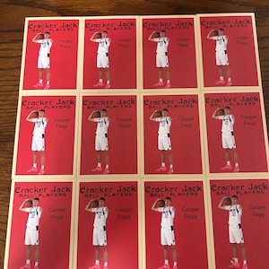 May include: A collection of Cracker Jack Ball Players trading cards featuring a basketball player in a white uniform with black accents and pink shoes. Each card has a red background and the player's name, Cooper Flagg.