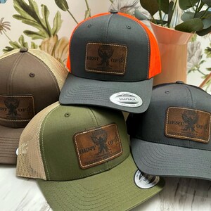 May include: Four trucker hats with a brown leather patch that says "Best Of" with a bird design. The hats are in different colours: brown, grey, green, and grey with orange mesh.