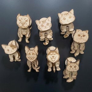 以下が含まれることがあります： レーザー刻印された様々な猫や犬のイラストが施された8つの木製動物マグネットのコレクション。各ピースは、暗い表面に配置され、詳細な顔の特徴と毛の質感を備えた、座った姿勢の異なる動物を描いています。