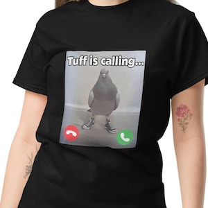 Könnte beinhalten: Ein schwarzes Kurzarm-T-Shirt mit einem Grafikdruck einer Taube, die schwarz-weiße High-Top-Sneaker trägt. Über dem Vogel steht der Text "Tuff is calling..." und darunter befinden sich rote und grüne Anrufsymbole auf hellem Grund.