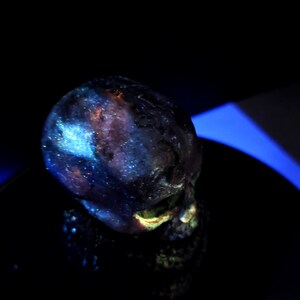 May include: A dark, glowing skull sculpture with a galaxy-like pattern of blues, purples, and oranges. The skull is set against a black background, with a hint of blue light.