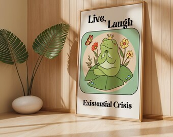 Puede incluir: Una rana verde con una corona sentada en posición de loto sobre una hoja verde con flores y una mariposa. El texto "Live, Laugh, Existential Crisis" está escrito en el cartel.