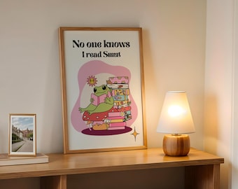 Puede incluir: Una impresión enmarcada con una rana verde sentada en un hongo leyendo un libro. La impresión tiene el texto "No one knows I read Smut".