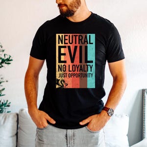 May include: Black t-shirt with the text "NEUTRAL EVIL NO LOYALTY JUST OPPORTUNITY" in a colorful rectangular design. A dragon graphic is at the bottom. The shirt is being worn by a person.