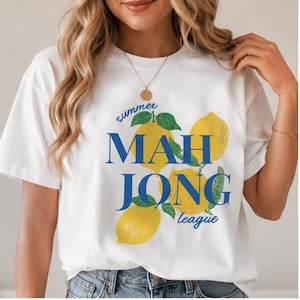 May include: A white t-shirt featuring a graphic print of three yellow lemons with green leaves. The text "summer" and "league" appear in blue script, while the words "MAH JONG" are printed in large, bold, blue capital letters across the center.