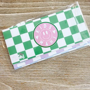 May include: A stack of stationery with a green and white checkered pattern. A pink circle with a smiley face and the words "KIDS MAH" is centered on the top sheet. The text "show mahj" is visible on the bottom sheet.