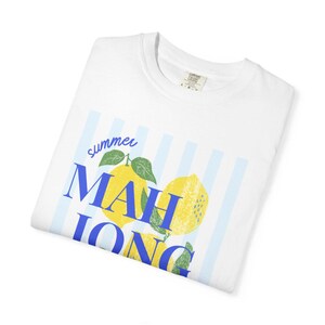 May include: A white short-sleeve t-shirt featuring a graphic of yellow lemons with green leaves over light blue vertical stripes. The text "summer" is written in blue script above the blue block-lettered word "MAHJONG" printed across the lemons.