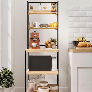 Puede incluir: Una estantería de cocina de metal negro con estantes de madera. La unidad tiene un microondas, una cafetera, tazas y otros artículos de cocina en los estantes. La unidad está en una cocina con un salpicadero de azulejos blancos.