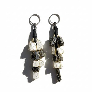 May include: Two keyrings featuring clusters of black and white stones. Each keyring has a silver ring attached to a black woven cord. The stones are encased in gold-coloured wire. The stones alternate between black and white.