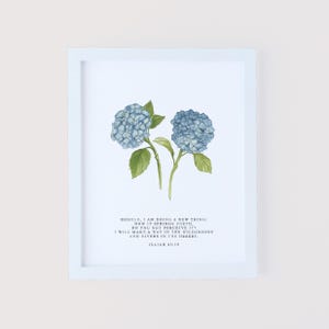 May include: A framed print featuring a watercolor illustration of two blue hydrangea flowers with green leaves. The print includes the text "BEHOLD, I AM DOING A NEW THING; NOW IT SPRINGS FORTH, DO YOU NOT PERCEIVE IT? I WILL MAKE A WAY IN THE WILDERNESS AND RIVERS IN THE DESERT. ISAIAH 43:19."