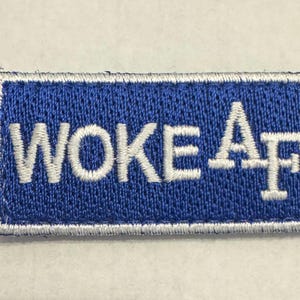 May include: Embroidered patch with the text "WOKE AF" in white lettering on a blue rectangular background. The patch has a white border.