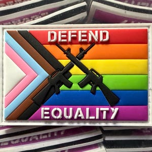May include: A rectangular patch with a white border features a rainbow flag design with two crossed black rifles. The words "DEFEND" and "EQUALITY" are in white block letters. The patch also includes the Progress Pride flag.