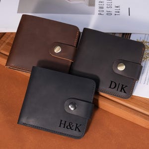 Op de afbeelding: Drie leren portemonnees in bruin, donkerbruin en zwart. Elke portemonnee heeft een druksluiting en gepersonaliseerde initialen. De donkerbruine portemonnee heeft "D|K" en de zwarte "H&K" gegraveerd.