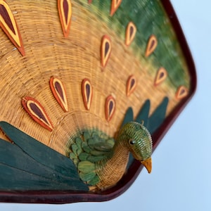 May include: A woven peacock wall hanging with a green and brown body and a fan of brown and green feathers. The peacock's head is green with a yellow beak.