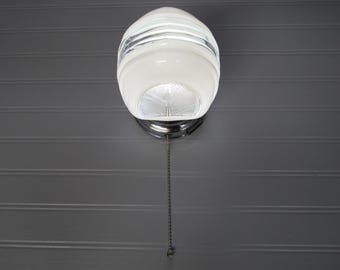 May include: A white ceiling light fixture with a pull chain. The light fixture has a round, frosted glass shade with a decorative pattern.