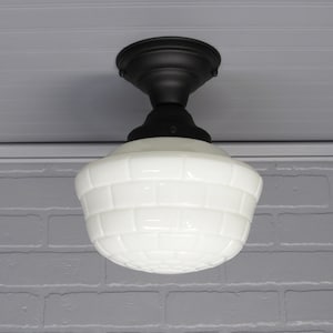 May include: A ceiling light fixture with a black base and a white, brick-patterned glass shade. The fixture is mounted on a white ceiling and is suitable for interior lighting.