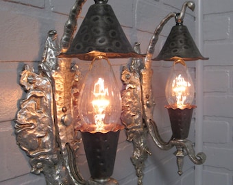 Könnte beinhalten: Zwei antike silberne Wandleuchten mit verzierten Designs und schwarzen Metallschirmen. Jede Leuchte hat eine klare Glühbirne mit warmem Licht.