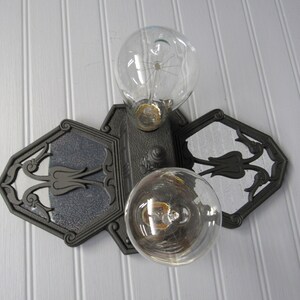 May include: A black metal light fixture with two clear glass light bulbs. The fixture has a decorative design with floral motifs.