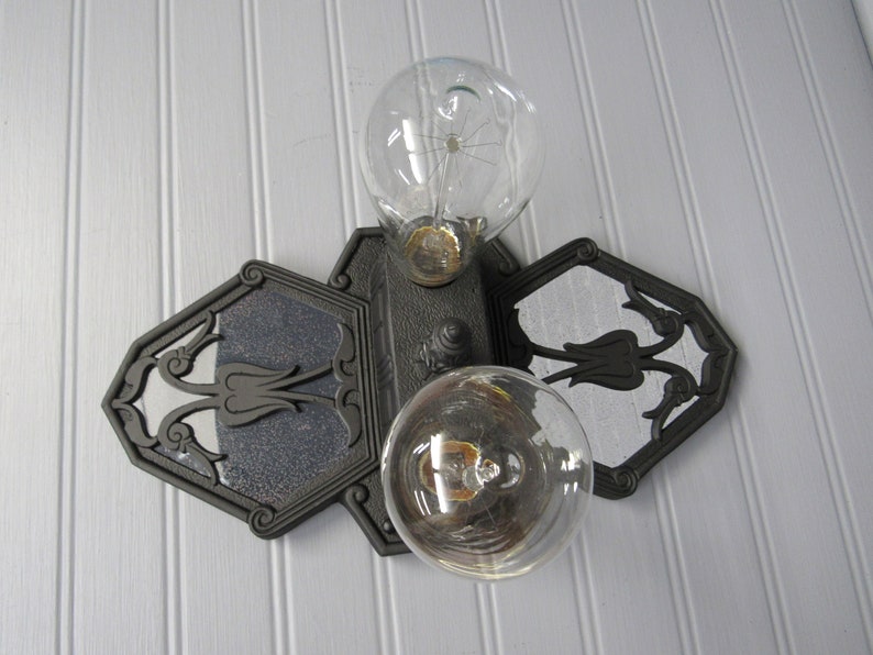 May include: A black metal light fixture with two clear glass light bulbs. The fixture has a decorative design with floral motifs.