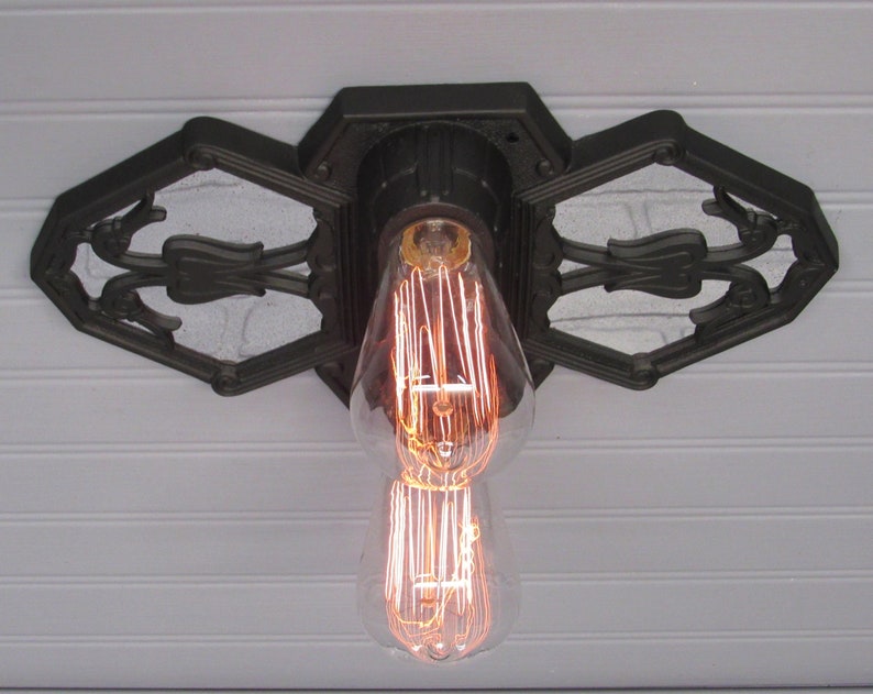 May include: A black cast iron ceiling light fixture with a decorative design. The fixture has a single light bulb with a filament design.