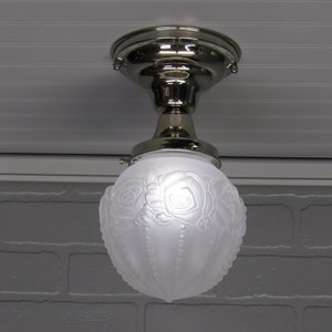 May include: A white frosted glass ceiling light fixture with a silver metal base and a floral design. The light fixture is hanging from a ceiling.