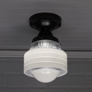 May include: A black ceiling light fixture with a white glass shade. The shade has a ribbed design and a frosted white finish.