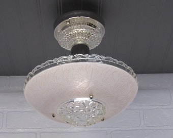 May include: A vintage ceiling light fixture with a pink glass shade featuring a floral design. The shade is surrounded by a clear glass rim with a beaded edge. The fixture has a chrome finish and a clear glass center piece with a beaded design.